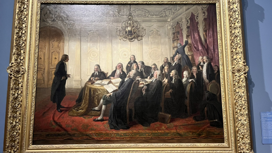 An oil painting of a lecture from the Early Modern period in a gilded frame. 